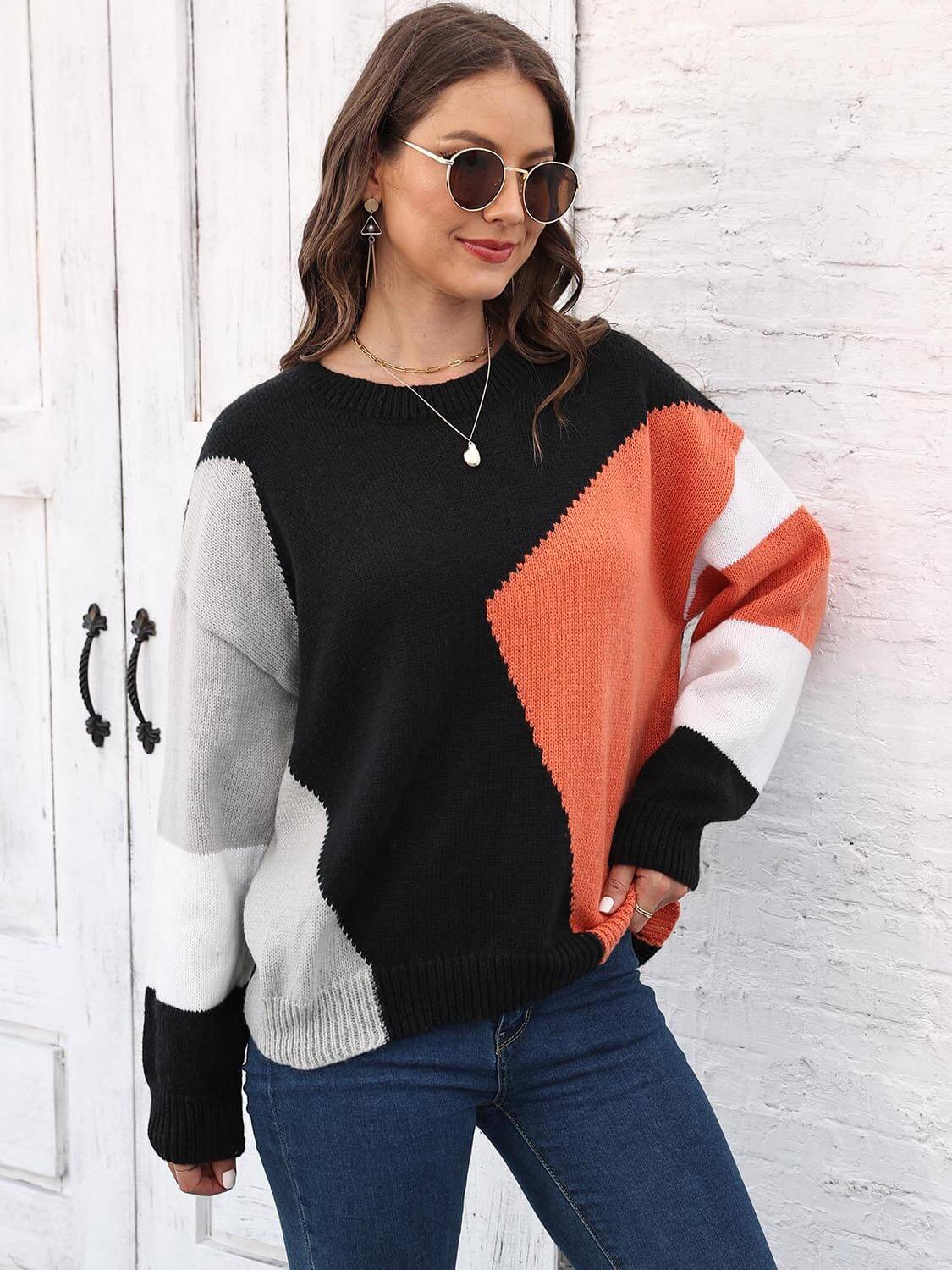 Model wearing a Color Block Round Neck Sweater with black, orange, and gray patterns, paired with jeans and sunglasses.