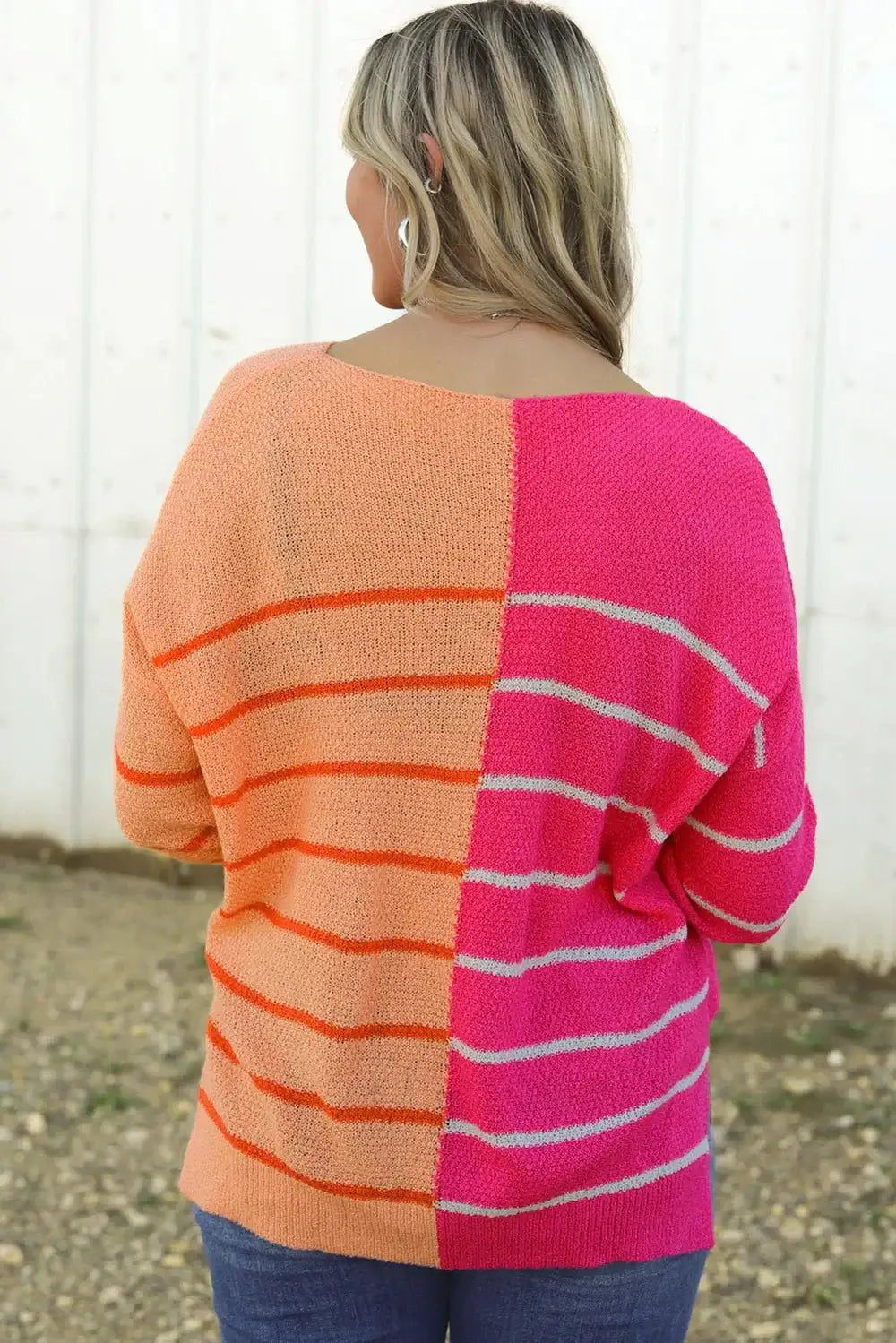 Back view of a woman wearing a Striped Pocketed Dropper Shoulder Sweater in orange and pink colors.